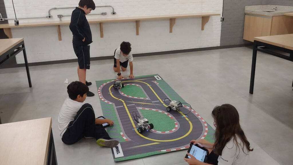Estudantes programando robôs LEGO em uma pista, na sala da DHEL